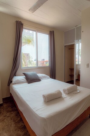 Ein Hotelzimmer mit Bett, Vorhängen, einem Fenster und einem Schrank.
