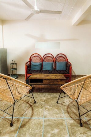 Ein Zimmer mit einem roten Korbsessel, zwei Korbstühlen, einem Holztisch und einem Deckenventilator.