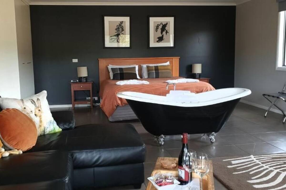 A modern bedroom with a large bed, a black bathtub, a leather sofa, and artwork on the walls.