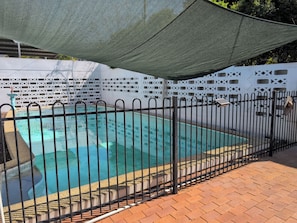 Ein Schwimmbecken mit schwarzem Metallzaun, umgeben von einer weißen Zierwand mit geometrischen Mustern.