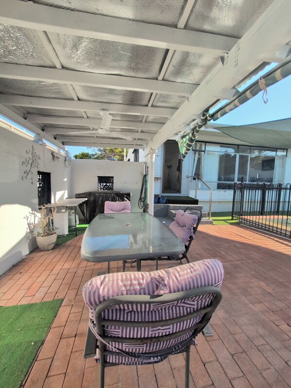Eine Außenpatio-Terrasse mit einem Glastisch, gestreiften Kissen, einem Grill und einer Überdachung.