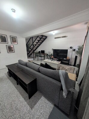 Ein modernes Wohnzimmer mit grauem Sofa, Fernseher, Treppe und Essbereich.