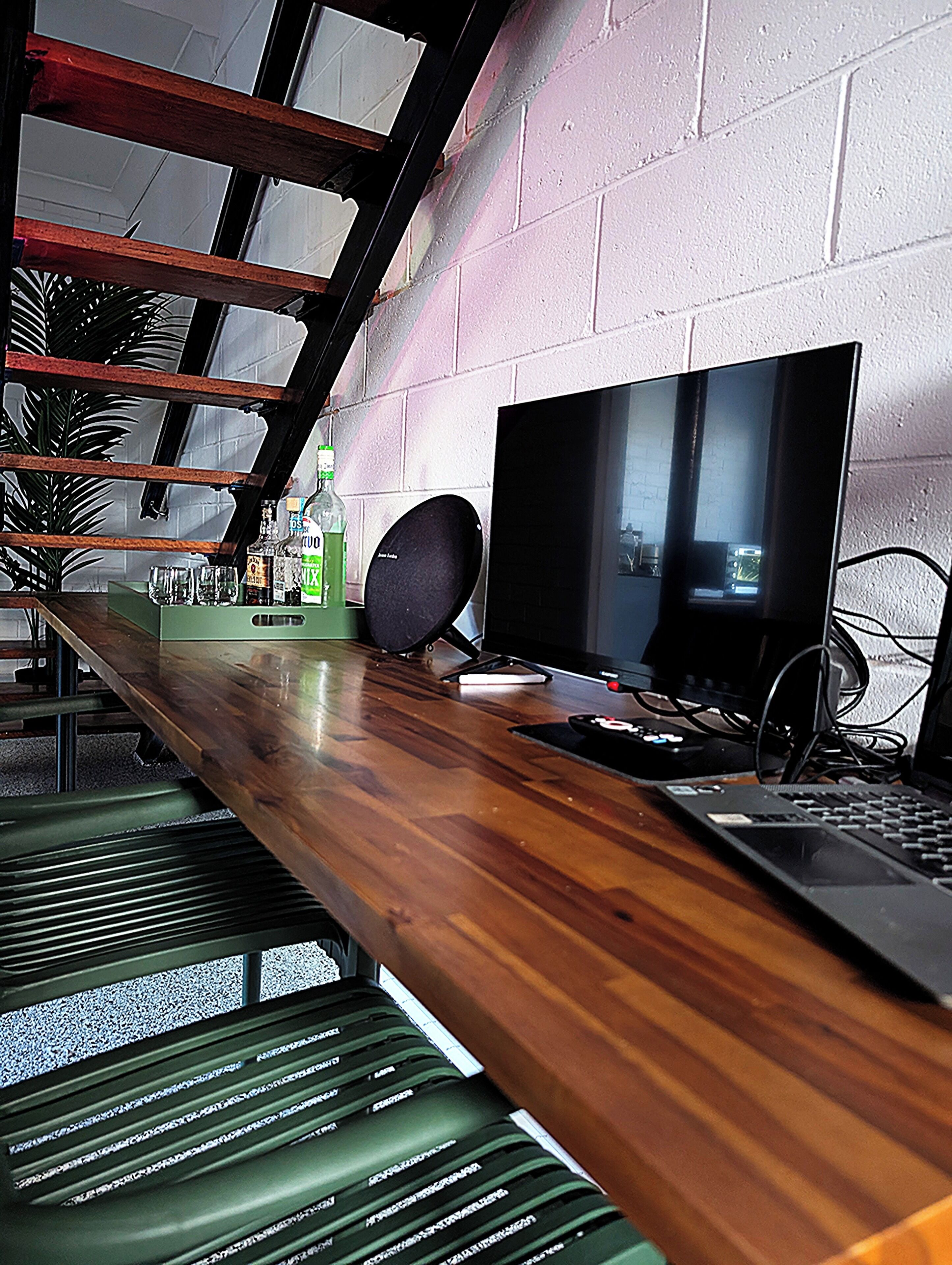 A modern bar area with a wooden counter, a television, and a bottle of liquor.