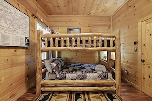 Un lit superposé avec une courtepointe matelassée et des oreillers, des murs en bois et une carte accrochée au mur.