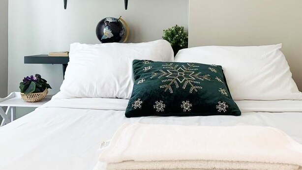 Un lit bien fait, avec du linge de lit blanc et un coussin décoratif vert, un globe terrestre et un tableau encadré, le tout placé sur une étagère noire au-dessus du lit.