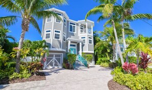 A two-story house with a front porch, a garage, and a staircase leading to the entrance. - Tropical Oasis ~ Rooftop Views/Games/Walk to Beach (Holmes Beach)