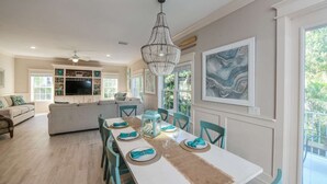 Een eetruimte met een witte tafel gedekt voor zes personen, teal stoelen en een kroonluchter.