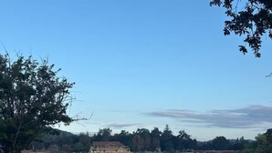Blick auf ein Seeufer mit einem großen Gebäude im Hintergrund, umgeben von Bäumen und einem klaren Himmel.