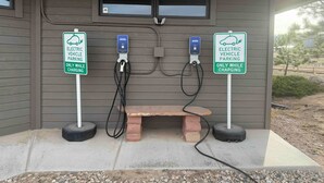 Una estación de carga para vehículos eléctricos con dos puntos de carga, un banco y una cámara de vigilancia.