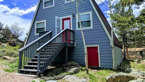 Una casa con techo inclinado, puerta roja y una escalera que conduce a la entrada.