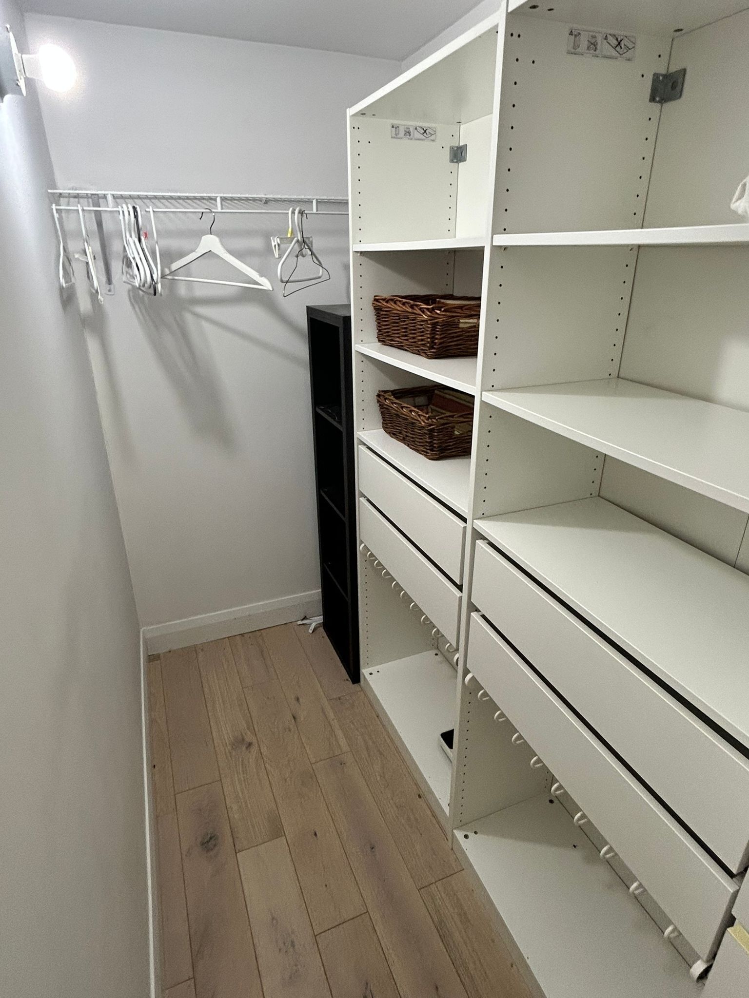 A walk-in closet with white shelving, a black hanging rack, and wooden flooring.