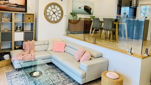 Una sala moderna con un sofá modular, una mesa de centro de vidrio y un comedor separado por una pared de vidrio.