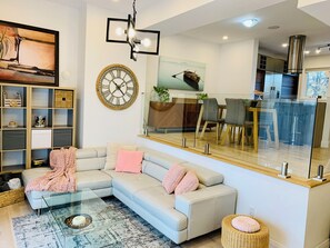 Una sala moderna con un sofá modular, una mesa de centro de vidrio y un comedor separado por una pared de vidrio.