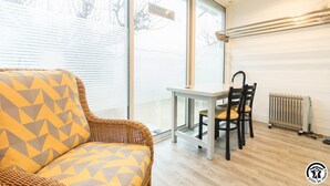 A room with a wicker sofa, a small table with chairs, a radiator, and large windows. - House Venitia T2 - AUSSONNE (AUSSONNE)