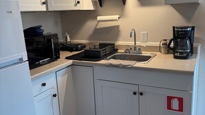 Pieni, käytännöllinen keittiö, jossa on valkoiset kaapit, ruostumattomasta teräksestä valmistettu pesuallas, kahvinkeitin ja mikroaaltouuni.