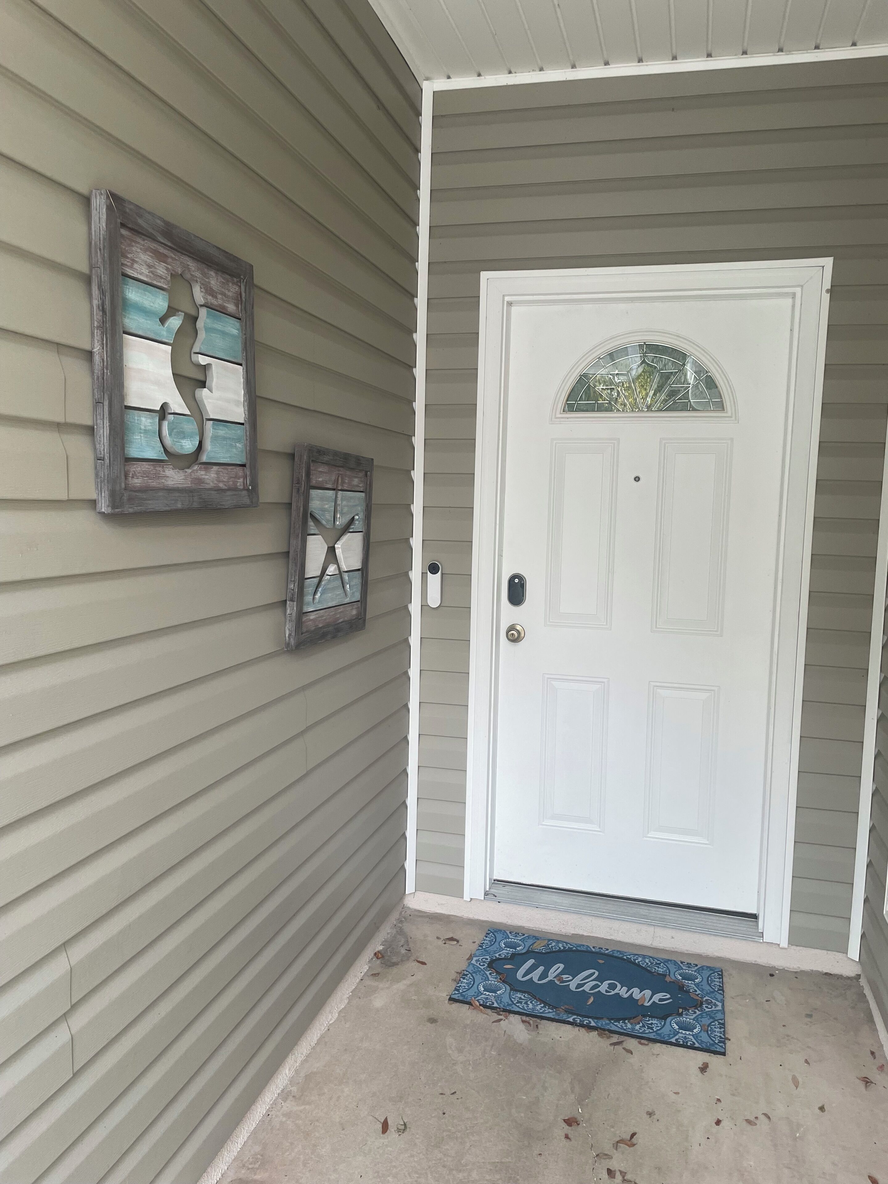 Une porte d’entrée avec un paillasson, un élément décoratif mural et une boîte aux lettres.