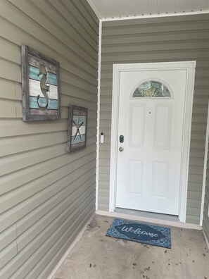 A front door with a welcome mat, a decorative wall piece, and a mailbox.