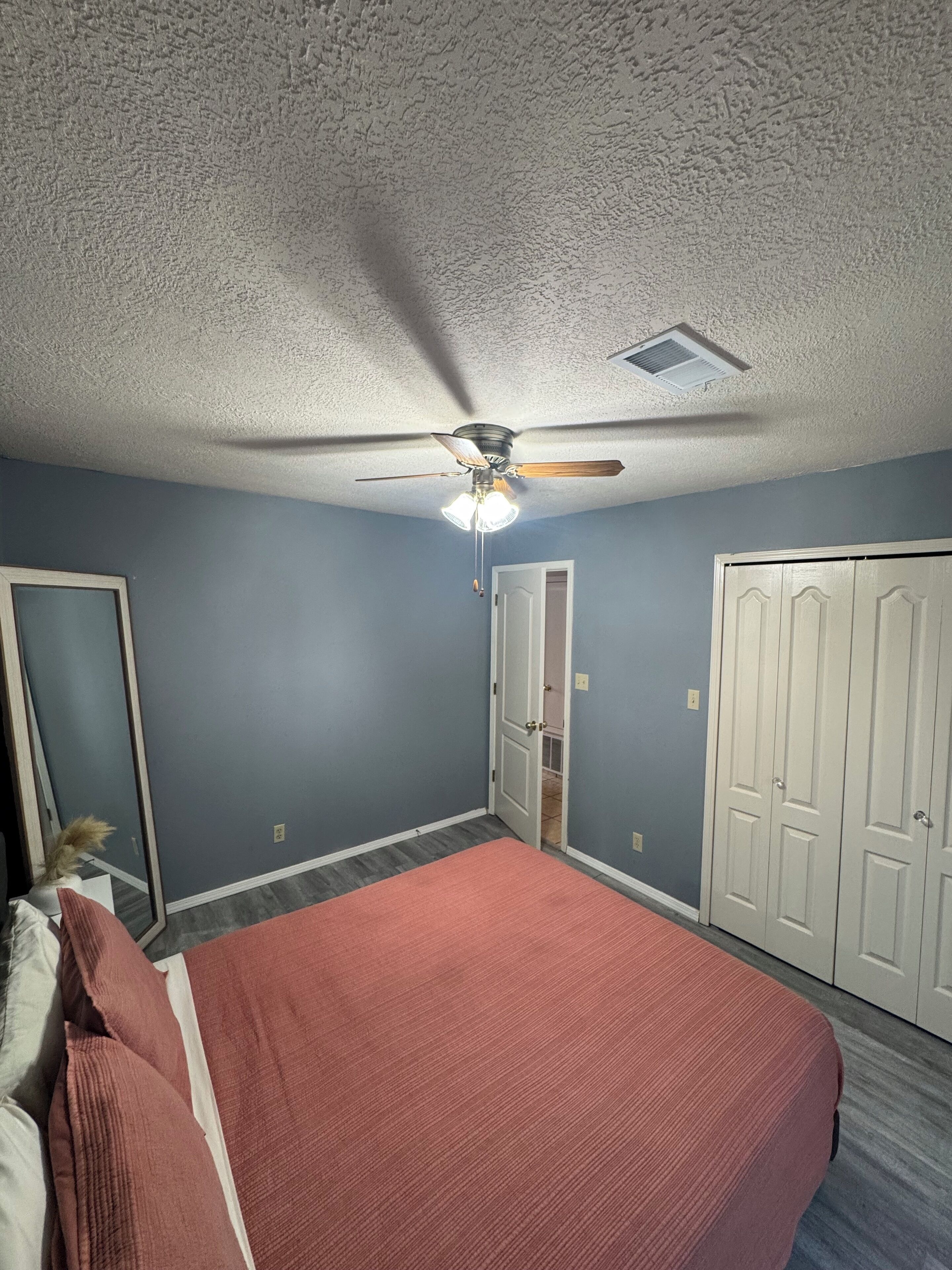 Une chambre à coucher avec un lit, un ventilateur de plafond, une porte et un placard.