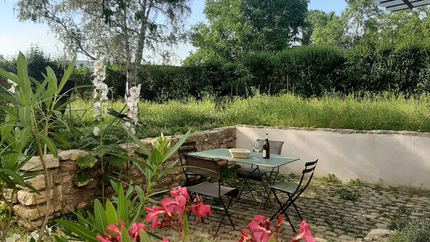 An outdoor seating area with a table and chairs, surrounded by greenery and flowering plants. - IDEAL FOR YOUR SPA TREATMENT IN SANTENAY (Chagny)