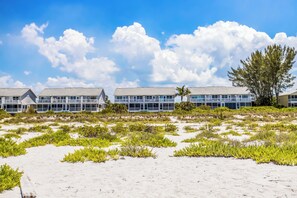 Ein Strandhotel mit mehrstöckigen Gebäuden, ein Sandstrand im Vordergrund und ein klarer, blauer Himmel mit Wolken.