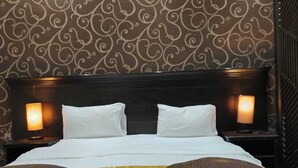 A hotel room with a large bed, two bedside lamps, and a patterned wallpaper. - asyl hotel (Taif)