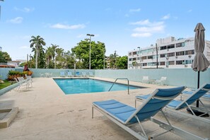 A swimming pool with lounge chairs, a covered umbrella, and a building in the background. - Caribe Aqua Loft  Steps to the Beach  3BR Condo (Isla Verde)