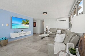 A modern living room with a flat-screen TV, a grey sofa, a coffee table, and a wall-mounted TV shelf. - Caribe Aqua Loft  Steps to the Beach  3BR Condo (Isla Verde)