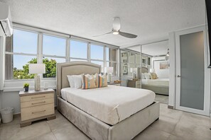 A bedroom with a bed, bedside tables, a ceiling fan, a window, and a door. - Caribe Aqua Loft  Steps to the Beach  3BR Condo (Isla Verde)