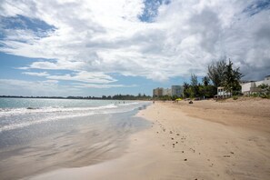 A beach with sand, water, and buildings in the background. - Caribe Aqua Loft  Steps to the Beach  3BR Condo (Isla Verde)