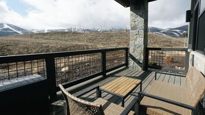 Un balcone con mobili in vimini, pilastri in pietra e vista sulle montagne innevate.