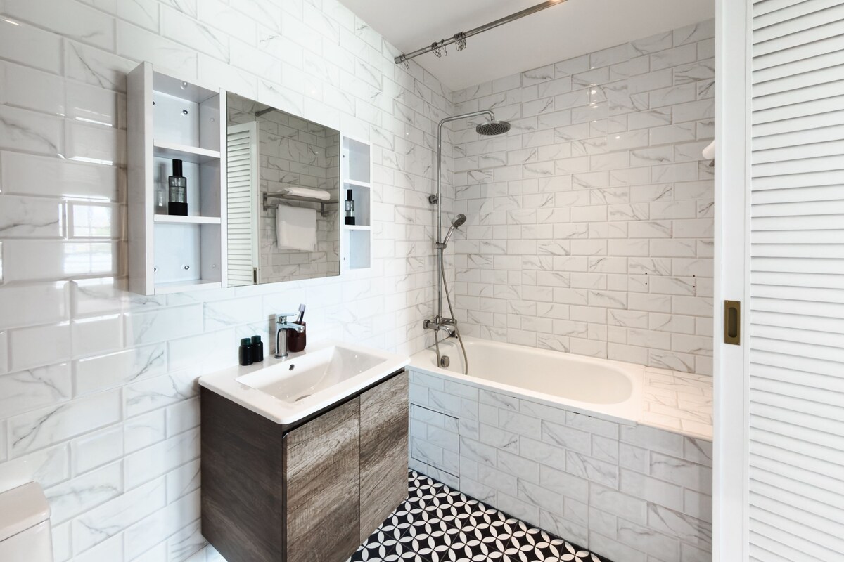 Een moderne badkamer met een marmeren wand, een houten wastafelmeubel, een witte wastafel en een vrijstaand bad.