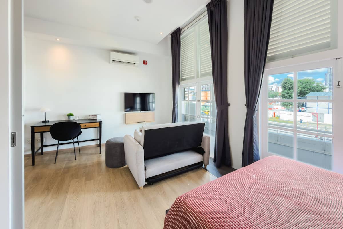 A modern hotel room with a sofa, a TV, a desk, and a large window with curtains.
