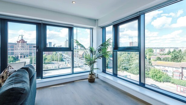 Um quarto espaçoso com grandes janelas, piso de madeira e um vaso de planta.