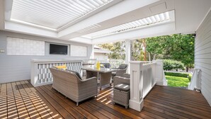 En overdækket terrasse med fletmøbler, et fladskærms-tv og udsigt til haven.