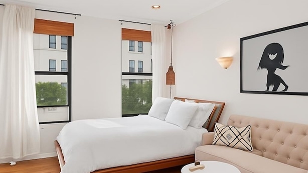 Un dormitorio moderno con una cama, un sofá, una mesa redonda y un ventanal con cortinas.