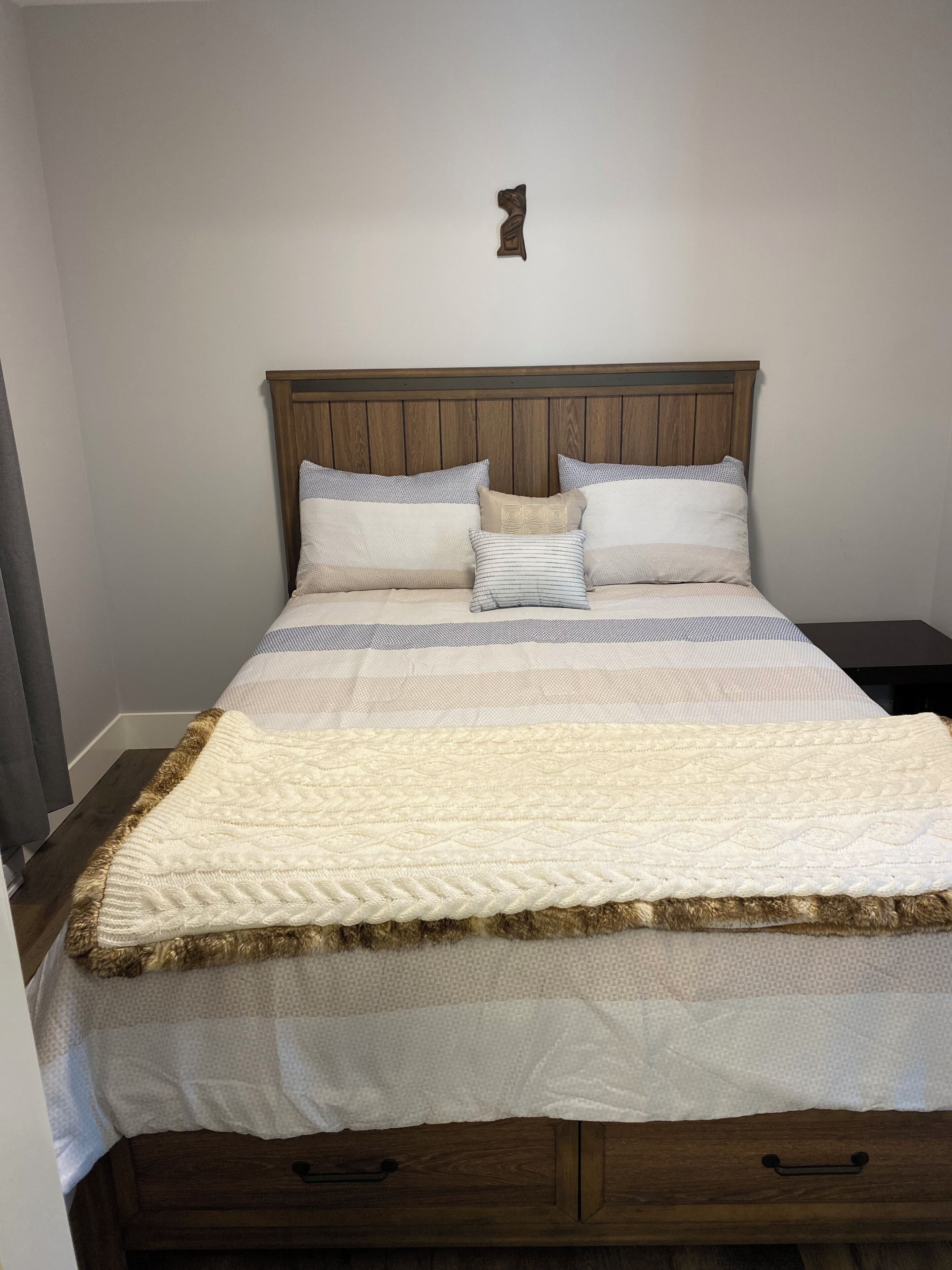 Un lit bien fait, avec une tête de lit en bois, plusieurs oreillers et une couette blanche.