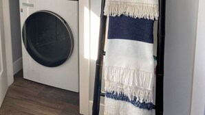 A laundry room with a washing machine and dryer, a black metal drying rack, and a framed picture on the wall.