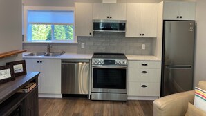 A modern kitchen with white cabinetry, stainless steel appliances, and a window with a view of greenery.