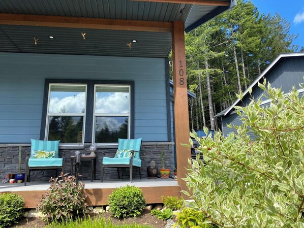 A house with a porch, two chairs, a table, and a potted plant.