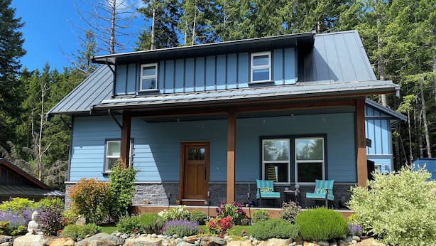 A two-story house with a stone foundation, a wooden door, and a porch with two chairs.