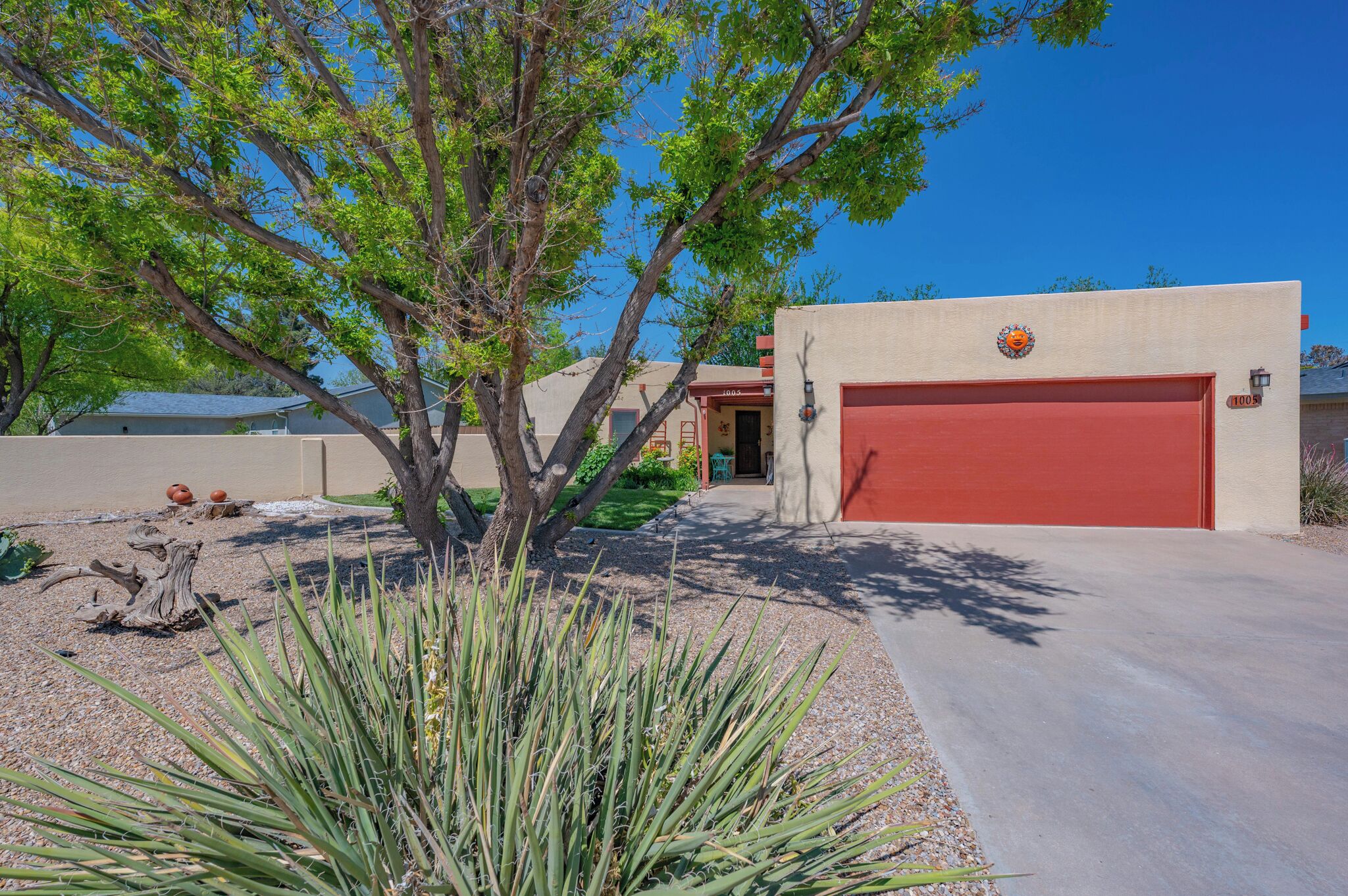 A red garage door with a logo, a tree, and agave plants in the foreground.