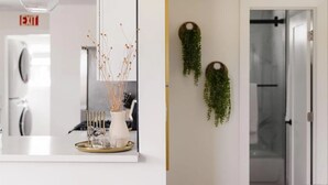 A modern kitchen with a white countertop, a clear glass vase with dried branches, and a gold tray with glasses. - Coastal Front Home in downtown Oceanside (Oceanside)