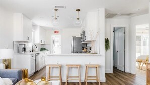A modern kitchen with white cabinets, a central island, and wooden stools. - Coastal Front Home in downtown Oceanside (Oceanside)