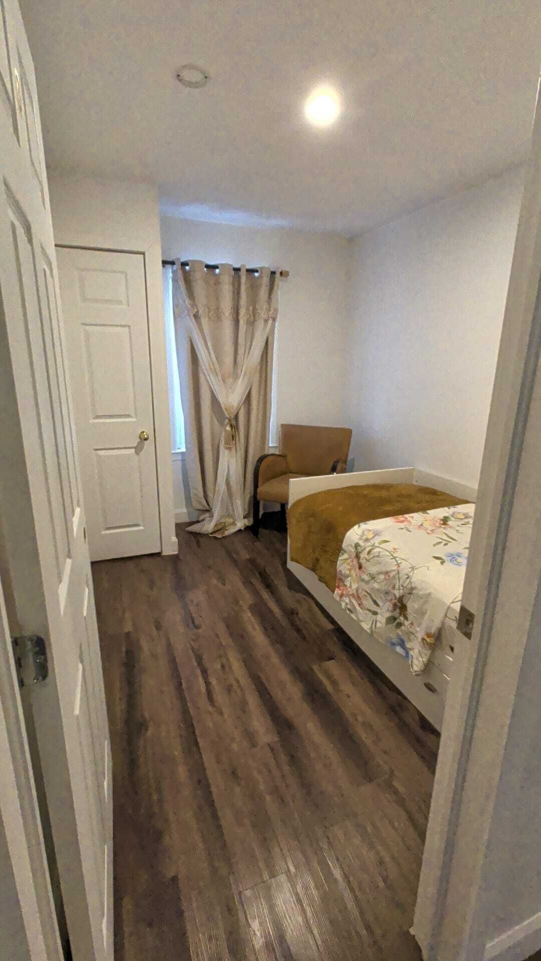 A bedroom with a bed, a chair, a door, and a window with curtains.