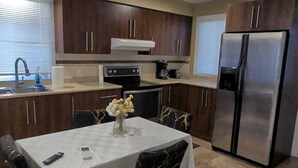 A modern kitchen with dark wooden cabinets, a stainless steel refrigerator, a dining table with a white tablecloth, and a vase of flowers.