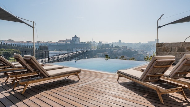 An infinity pool with lounge chairs on a wooden deck, overlooking a cityscape and a bridge. - Guestready - D. Hugo Boutique Hotel B&B (Porto)