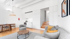 A modern living room with a grey sofa, a round wooden coffee table, and a dining area with a wooden table and chairs. A kitchen is visible in the background with white cabinets and a wooden staircase. - Guestready - D. Hugo Boutique Hotel B&B (Porto)