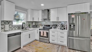 A modern kitchen with white cabinets, stainless steel appliances, a dishwasher, and a refrigerator. - Charming 3-bedroom home with hot pool and spa. (Clearwater)