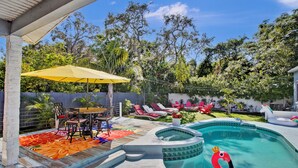 A backyard with a swimming pool, lounge chairs, a dining area, and a covered patio. - Charming 3-bedroom home with hot pool and spa. (Clearwater)