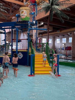 Parque acuático interior con un tobogán de agua, piscina y zona de juegos.